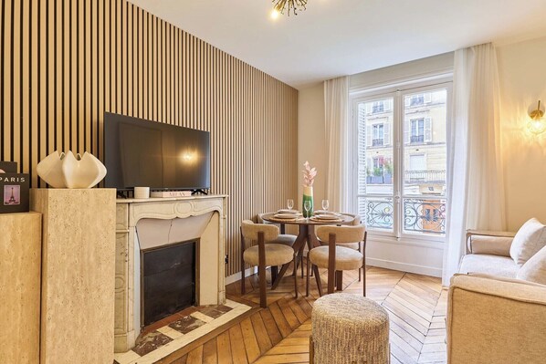 Una sala de estar moderna con chimenea, televisor, mesa de comedor con sillas y un ventanal con vistas a edificios.