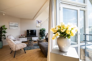 Una sala de estar moderna con un sofá, un televisor, una planta y una ventana con vistas.