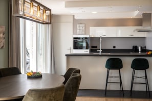 Une cuisine moderne avec des armoires blanches, une hotte en acier inoxydable et un coin repas comprenant une table ronde et deux tabourets de bar.