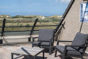 Una terraza con dos sillas grises acolchadas y una mesita pequeña, con vistas a un paisaje costero.