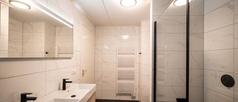A modern bathroom with a glass shower enclosure, a white vanity with a mirror, and a towel rack.