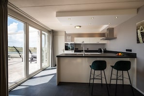 Une cuisine moderne dotée d’un grand îlot central, de deux tabourets de bar, d’une fenêtre offrant une belle vue et d’un plafond pourvu d’un éclairage encastré.