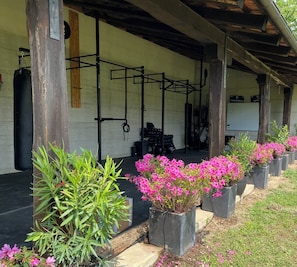 Un espace de remise en forme extérieur abrité, équipé de matériel d’exercice, de poutres en bois et de plantes en pot.