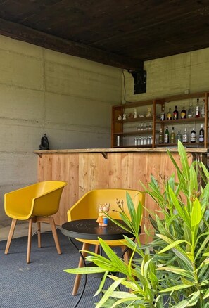 A bar area with wooden shelves, a round table, and two yellow chairs. - Private property, two houses, gym, pool and outside bar in stunning surrounding (Bosia Cuneo)