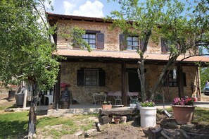 Un bâtiment en pierre avec un toit en tuiles, des places assises à l’extérieur et des plantes en pot.