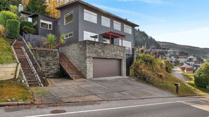 A modern two-story house with a stone facade, a garage, and a staircase leading to the entrance. - Alpine 75 Estate - Queenstown Hill 7 Bed (Queenstown)
