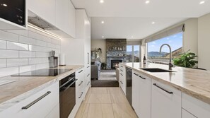 A modern kitchen with white cabinetry, a stone fireplace, and a view of the mountains. - Alpine 75 Estate - Queenstown Hill 7 Bed (Queenstown)