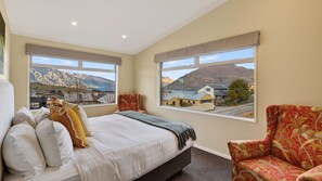 A bedroom with a bed, two windows, a chair, and a view of mountains and a lake. - Alpine 75 Estate - Queenstown Hill 7 Bed (Queenstown)