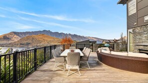 A wooden deck with outdoor furniture, a stone wall, and a view of mountains and a lake. - Alpine 75 Estate - Queenstown Hill 7 Bed (Queenstown)