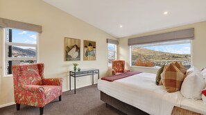 A bedroom with a bed, two chairs, a small table, and two paintings. - Alpine 75 Estate - Queenstown Hill 7 Bed (Queenstown)