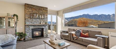 A living room with a stone fireplace, a sofa, a coffee table, and a large window with a mountain view.