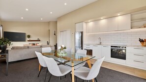 A modern kitchen with white cabinetry, a glass dining table, and a built-in oven. - Alpine 75 Cottage - Queenstown Hill 2 Bed (Queenstown)