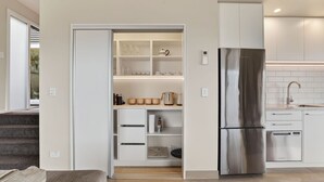 A modern kitchen with a built-in refrigerator, a countertop with a sink, and a pantry with glassware and kitchenware. - Alpine 75 Cottage - Queenstown Hill 2 Bed (Queenstown)