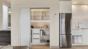 Eine moderne Küche mit Einbaukühlschrank, einer Arbeitsplatte mit Spüle und einem Vorratsschrank mit Gläsern und Geschirr.