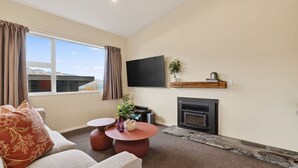 A living room with a fireplace, a flat-screen TV, a coffee table, and a sofa. - Alpine 75 Cottage - Queenstown Hill 2 Bed (Queenstown)