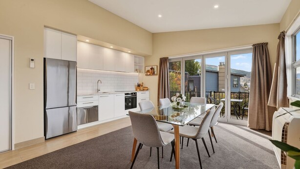 A modern kitchen with white cabinets, stainless steel appliances, and a dining area with a glass table and chairs. - Alpine 75 Cottage - Queenstown Hill 2 Bed (Queenstown)