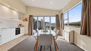 A modern kitchen with white cabinets, a dining table with chairs, and a view of mountains through large windows. - Alpine 75 Cottage - Queenstown Hill 2 Bed (Queenstown)