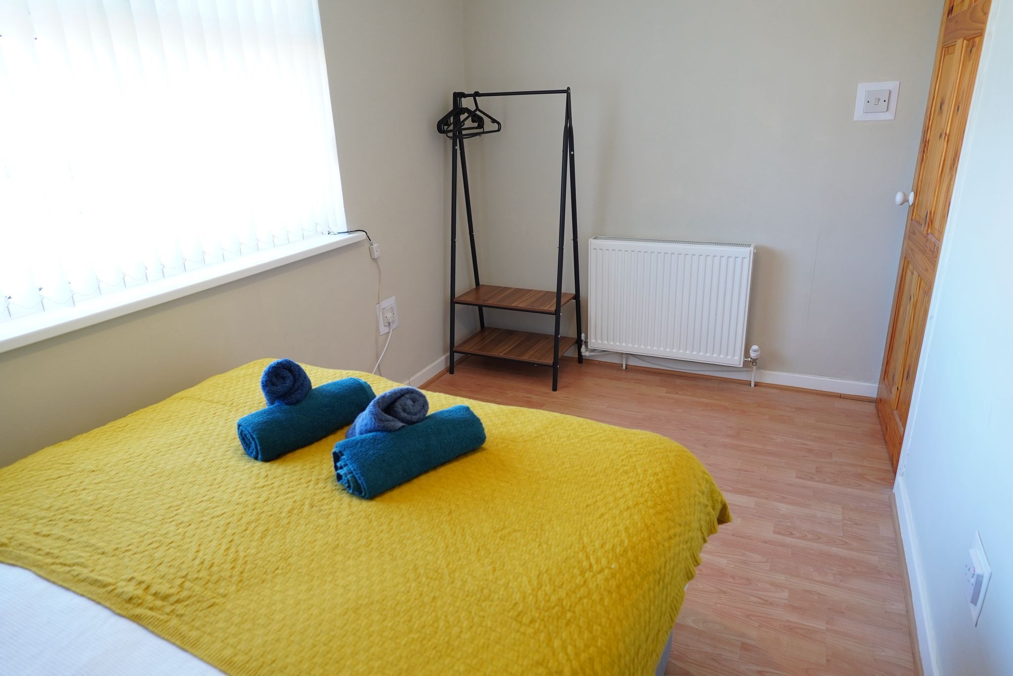 A room with a bed, a radiator, a wooden floor, and a window with blinds.