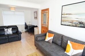 A living room with a sofa, a dining table, and a chair. There is a window with blinds, a door with a mirror, and a painting on the wall. - Princetown Palace, Free Parking (Sunderland)