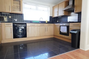 A kitchen with a washing machine, a stove, and a trash bin. - Princetown Palace, Free Parking (Sunderland)