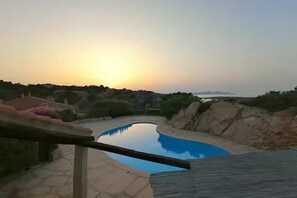 Ein Pool mit geschwungener Kante, umgeben von einer Holzterrasse und einer Steinmauer.