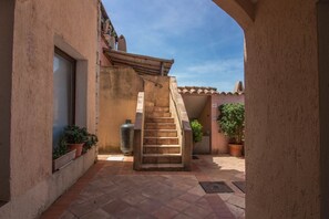 Une cour intérieure avec un escalier, des plantes en pot et un sol carrelé.