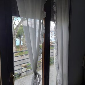 A door with a curtain tied at the bottom, a metal handle, and a view of a paved area with trees and a fence. - House Laguna Venice Garden, balconies, beach, families, bike, Venice, bus (Lido)