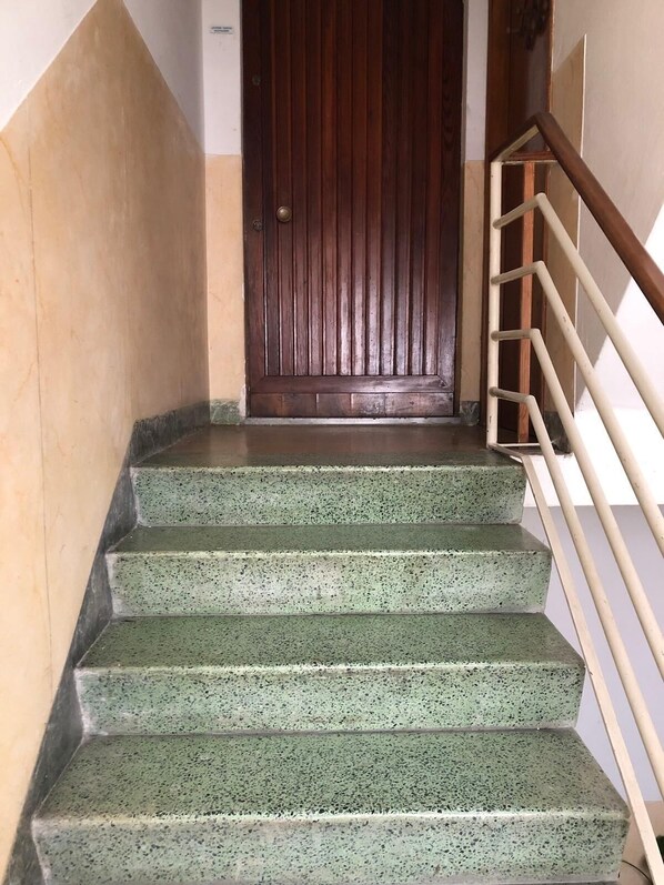Una escalera verde con motas que conduce a una puerta de madera, con una barandilla de metal a la derecha.