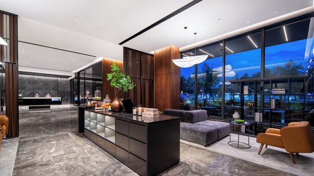 A modern lobby with a reception desk, a central island with a plant, a seating area with a sofa and armchairs, and a large window with a view of the city. - ZhongShan InterCity Expo Center Hotel (Zhongshan)