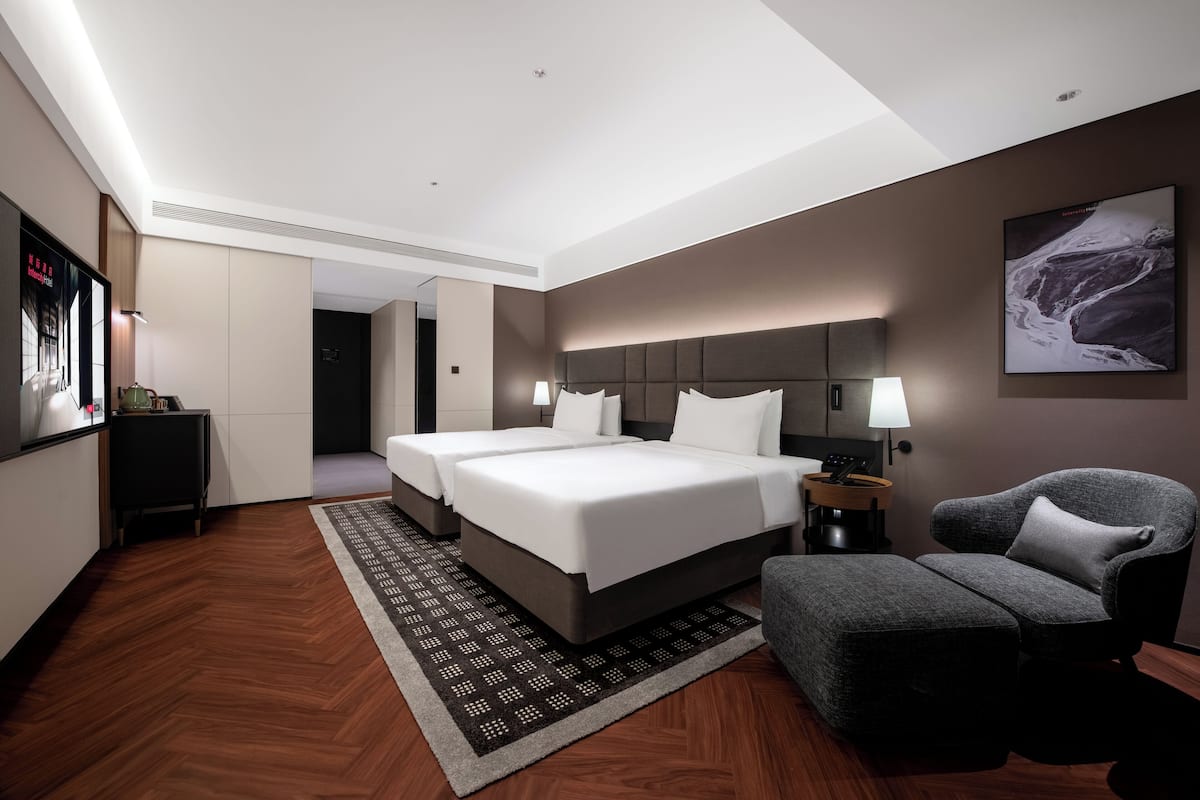 A modern hotel room with a large bed, two bedside tables, a chair, and a wall-mounted TV.