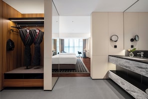 Une chambre d’hôtel moderne comprenant un lit, une salle de bain avec un miroir et un lavabo, et un dressing avec des vêtements suspendus.