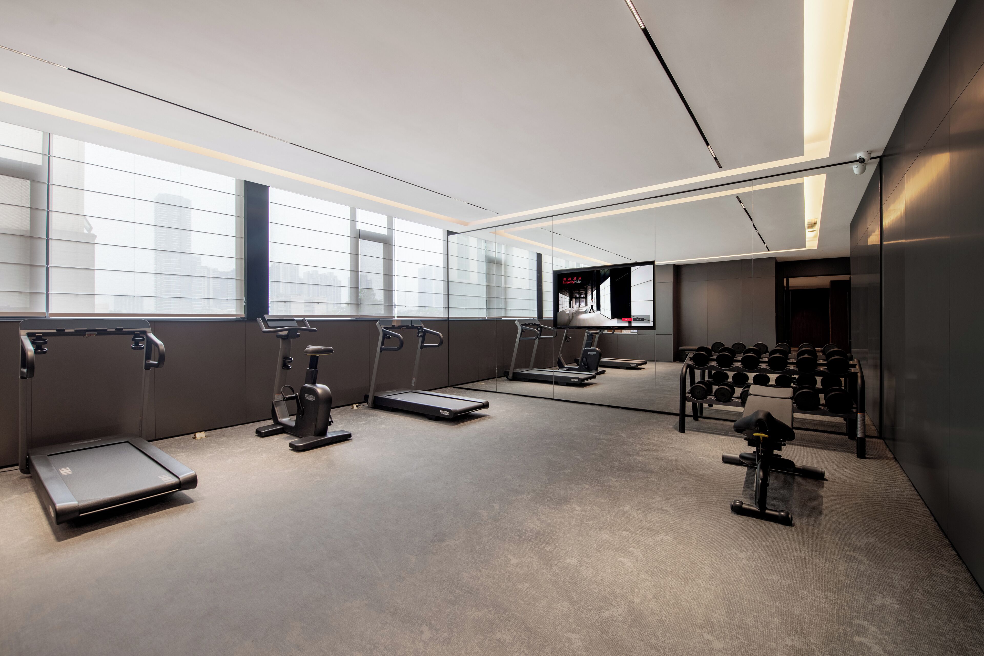 A modern gym with exercise equipment, large windows, and a mirrored wall.