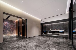 Um hall moderno com piso de mármore, balcão de recepção e uma parede grande com textura.