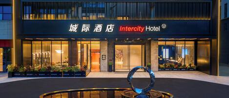 Un hotel con fachada moderna, una entrada destacada y una fuente decorativa al frente.