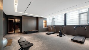 A modern gym with exercise equipment, a bench, and a large window providing natural light. - ZhongShan InterCity Expo Center Hotel (Zhongshan)