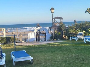 A beachside view with a gazebo, lounge chairs, and a gate leading to the beach. - Casita in Marina Puerto Cabopino with Shared Pool, Beachfront, Wi-Fi, Air Conditioning (Marbella)
