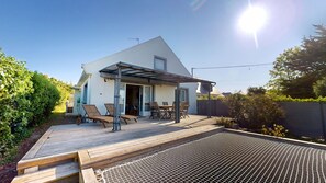 Ein modernes Haus mit Terrasse, Sitzgelegenheiten im Freien und einem überdachten Bereich.