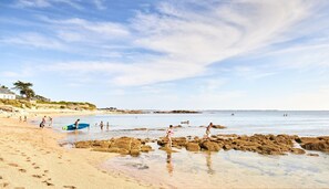 Ein Strand mit klarem Wasser, Felsen und Menschen bei verschiedenen Aktivitäten.