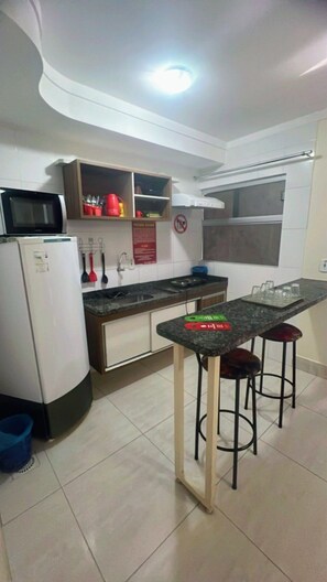 A compact kitchen with a microwave, stove, and a small dining area with stools. - HOTEL LACQUA DI ROMA (Caldas Novas)
