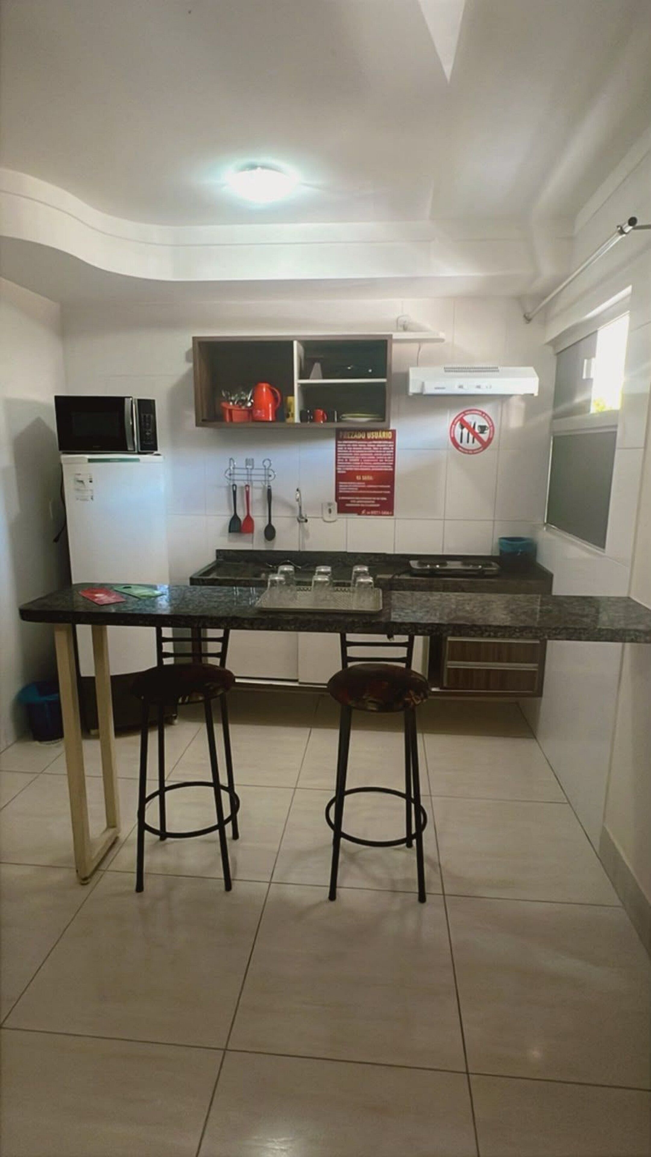 Cozinha compacta com micro-ondas, fogão e dois banquinhos.