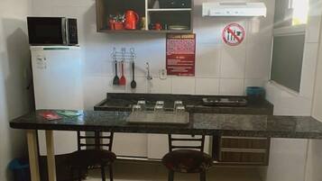 Cozinha compacta com micro-ondas, fogão e dois banquinhos.