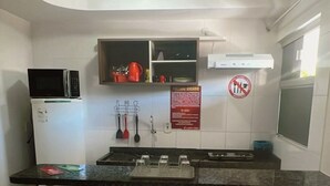 A compact kitchen with a microwave, a refrigerator, a sink, and a stove. There are utensils hanging on the wall and a sign indicating a no-food area. - HOTEL LACQUA DI ROMA  (Caldas Novas)