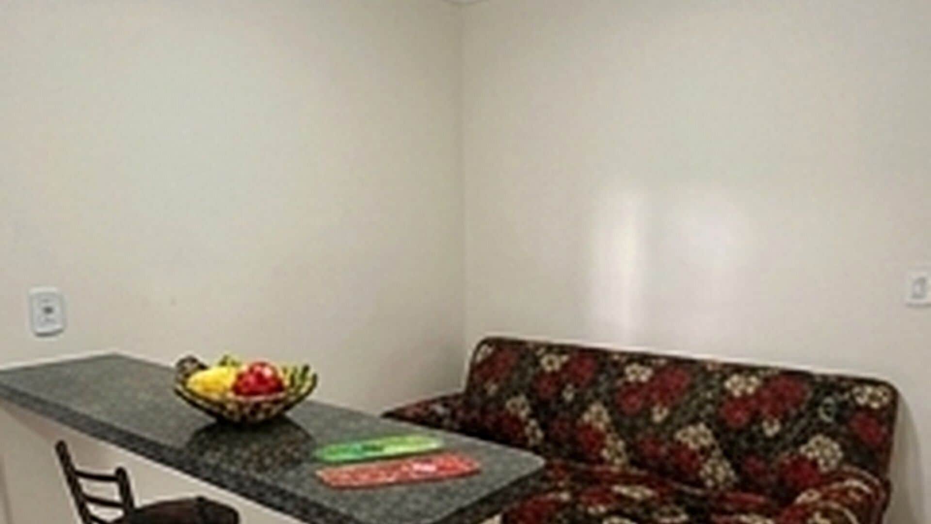 Una pequeña kitchenette con mostrador, un cuenco de fruta y un sofá estampado.