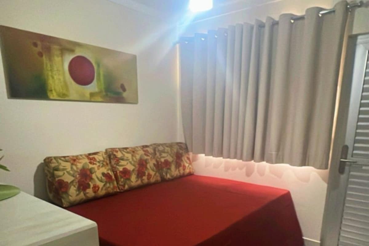 A room with a bed, a small table, a painting on the wall, and a door with curtains.