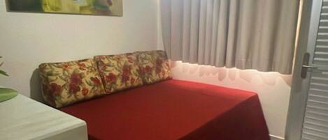 Una habitación con cama, una mesita, un cuadro en la pared y una puerta con cortinas.