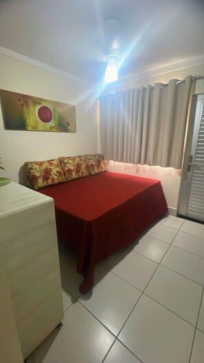 A room with a bed, a small table, a painting on the wall, and a door with curtains. - HOTEL LACQUA DI ROMA (Caldas Novas)