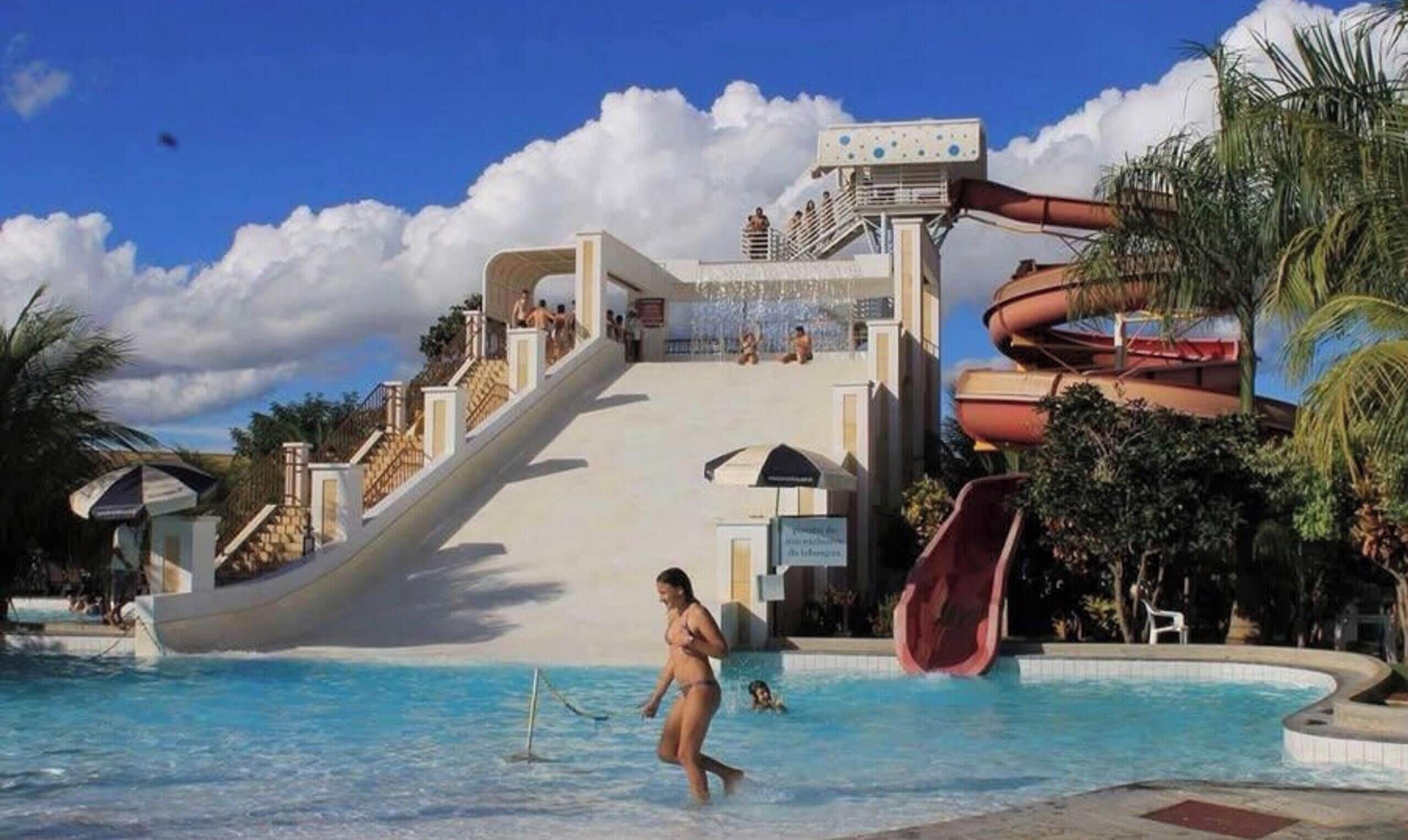 Un parque acuático con un tobogán grande, una piscina y palmeras.