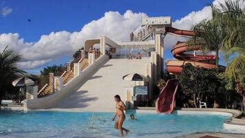 Un parque acuático con un tobogán grande, una piscina y palmeras.