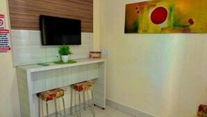 A compact living space with a kitchenette, a flat-screen TV, a ceiling fan, and a floral-patterned sofa. - HOTEL LACQUA DI ROMA  (Caldas Novas)