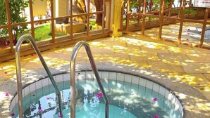 A hot tub with metal steps and a tiled edge, surrounded by a wooden fence and a paved area with scattered flower petals. - HOTEL LACQUA DI ROMA  (Caldas Novas)